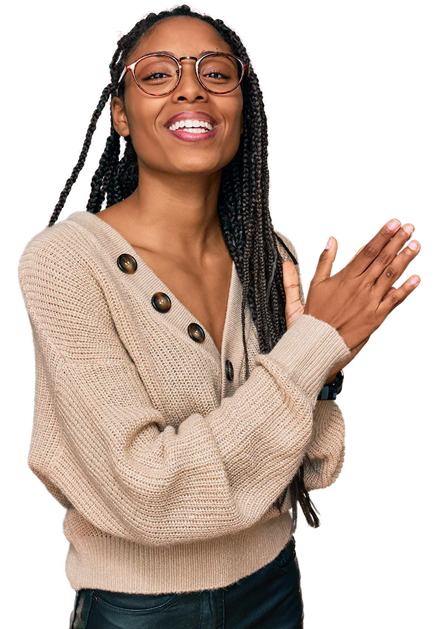 woman with long braided hair smiling clapping her hands together looking at the camera. She is wearing glasses and wearing a button up beige shirt.