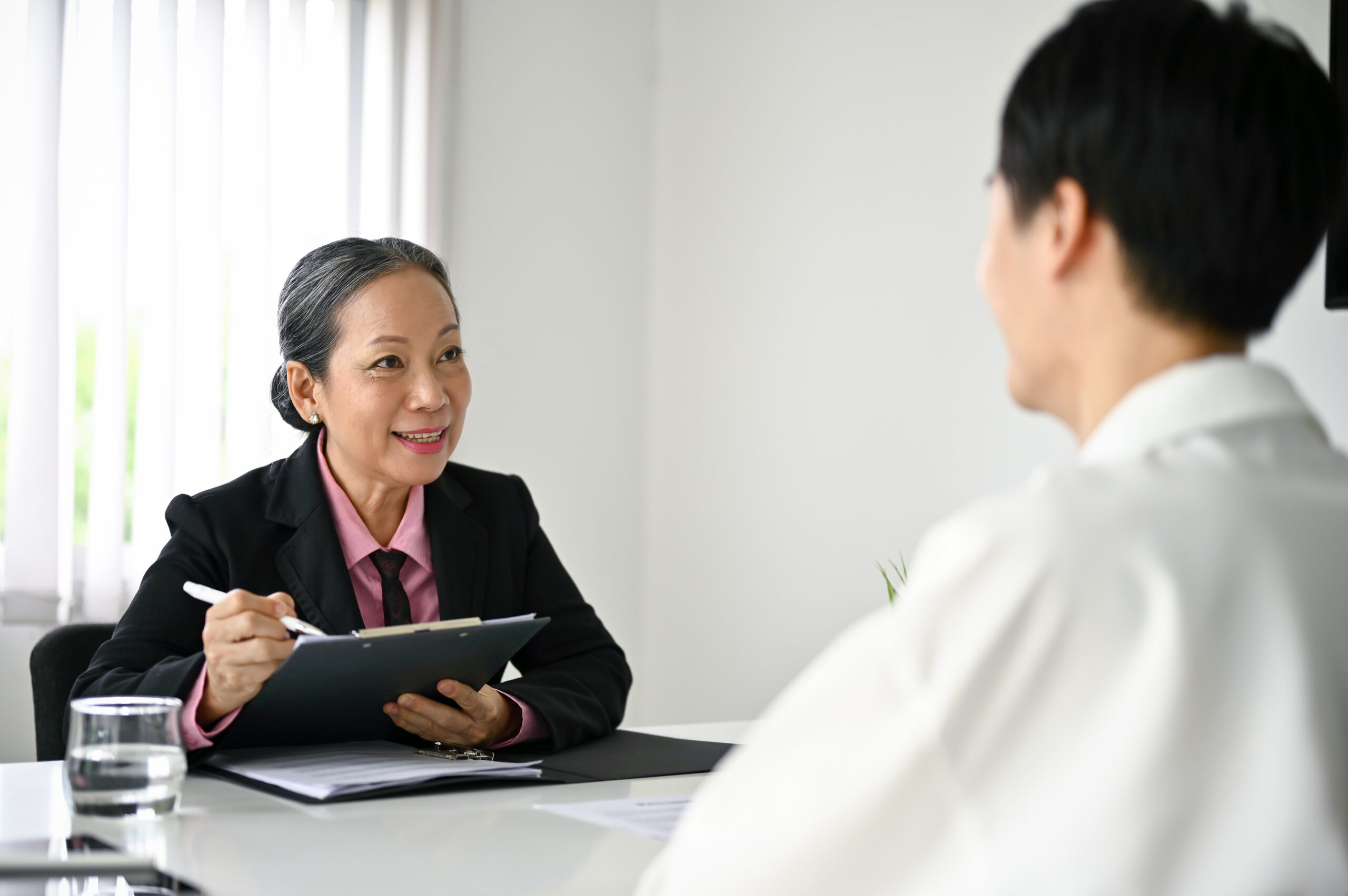 woman on her ipad in a black blazer sitting at a table across from a male in a white shirt